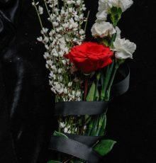 A moody bouquet featuring red and white flowers symbolizing loss on a black fabric background.